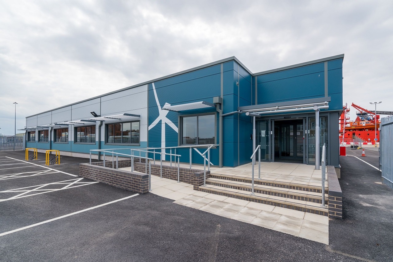 A modern building with a blue facade, featuring a wind turbine design, surrounded by a parking area.