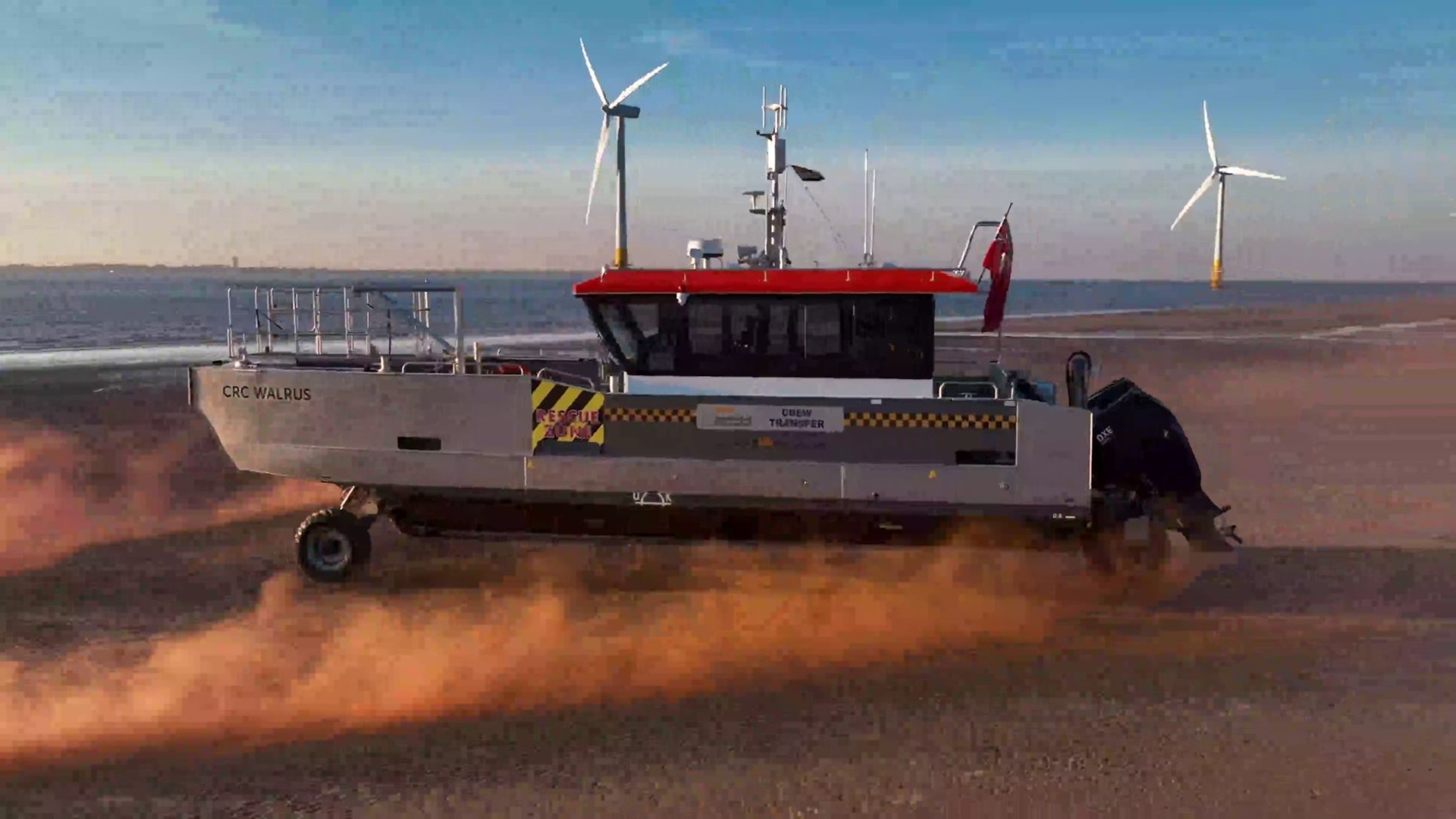 A boat named 'CRC Walrus' on sandy terrain with wind turbines and water in the background.