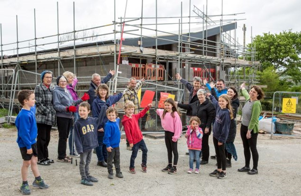 Group of people smiling and pointing at a construction site with scaffolding and a building.