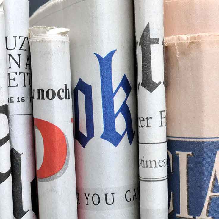 A collection of rolled-up newspapers showcasing various headlines and typography. The papers display a mix of fonts and colours.