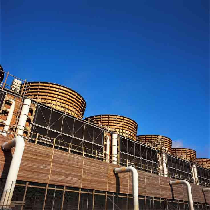 A row of large cooling towers against a clear blue sky, with pipes and a wooden panel structure.