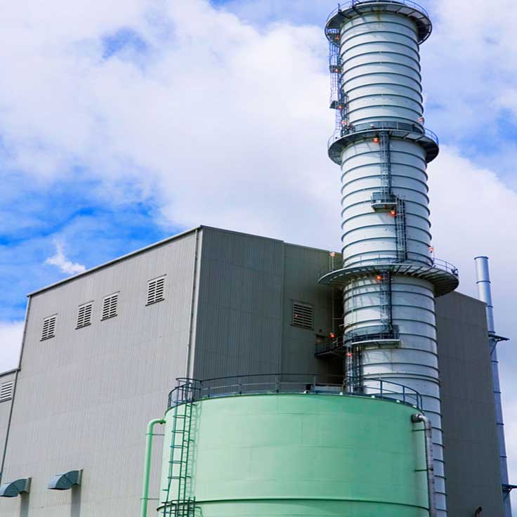 A large industrial structure with a tall, spiralled chimney and a green tank, under a blue sky with scattered clouds.