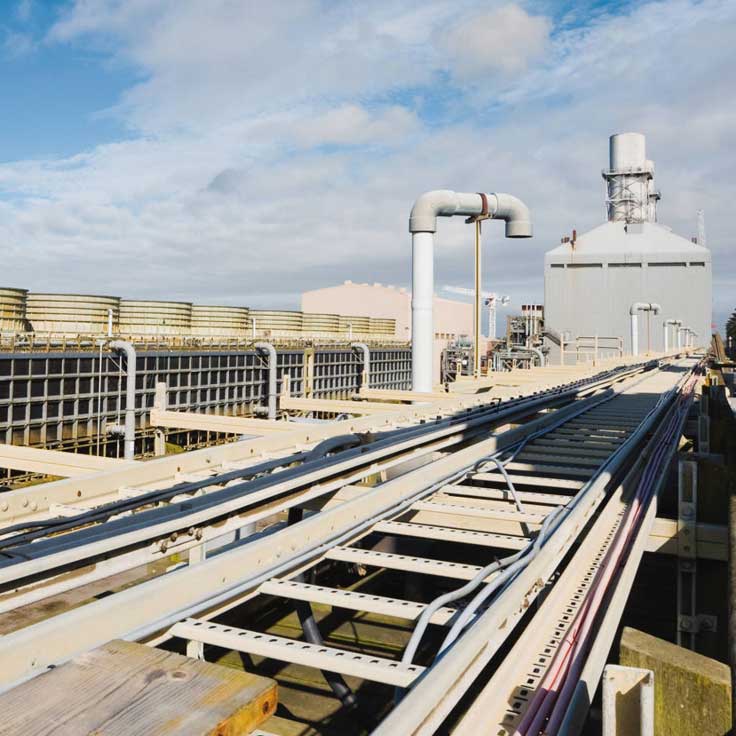 A view of industrial infrastructure with rail tracks, pipes, and large machinery under a partly cloudy sky.