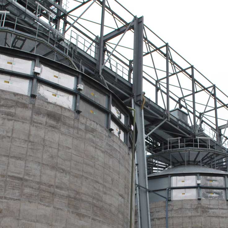 Close-up view of large industrial silos with a steel framework and concrete bases.