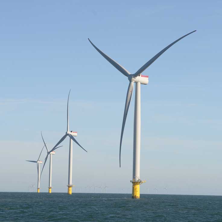 A series of wind turbines stand tall in the ocean under a clear blue sky, showcasing renewable energy technology.