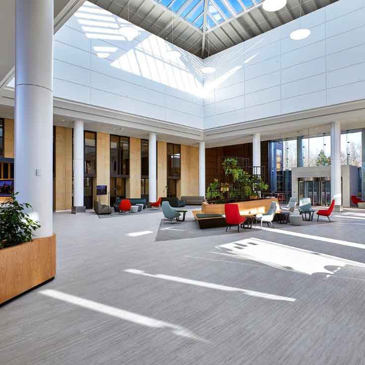 A spacious, modern atrium with a glass roof, featuring colourful seating and indoor plants.