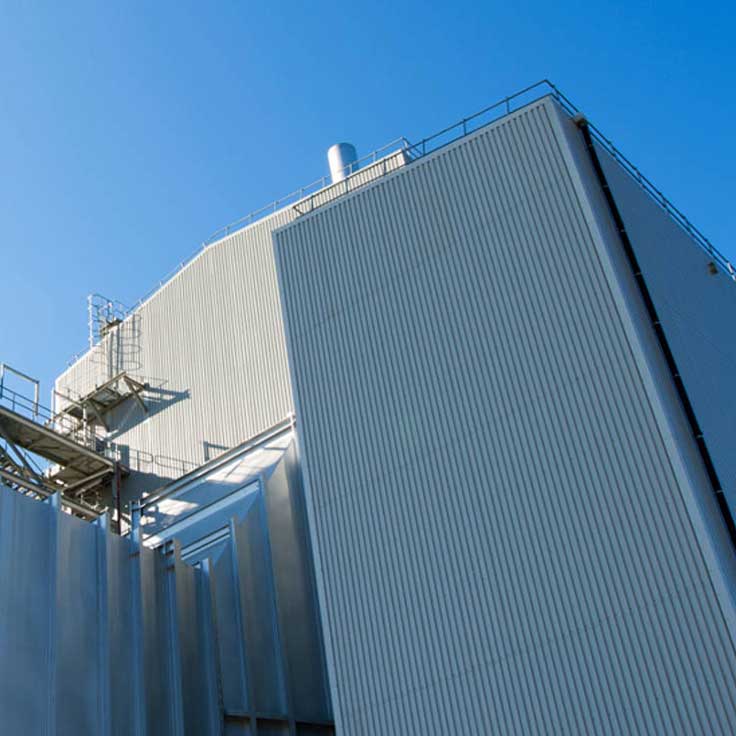 A tall industrial building with ribbed metal siding, a staircase, and a clear blue sky in the background.