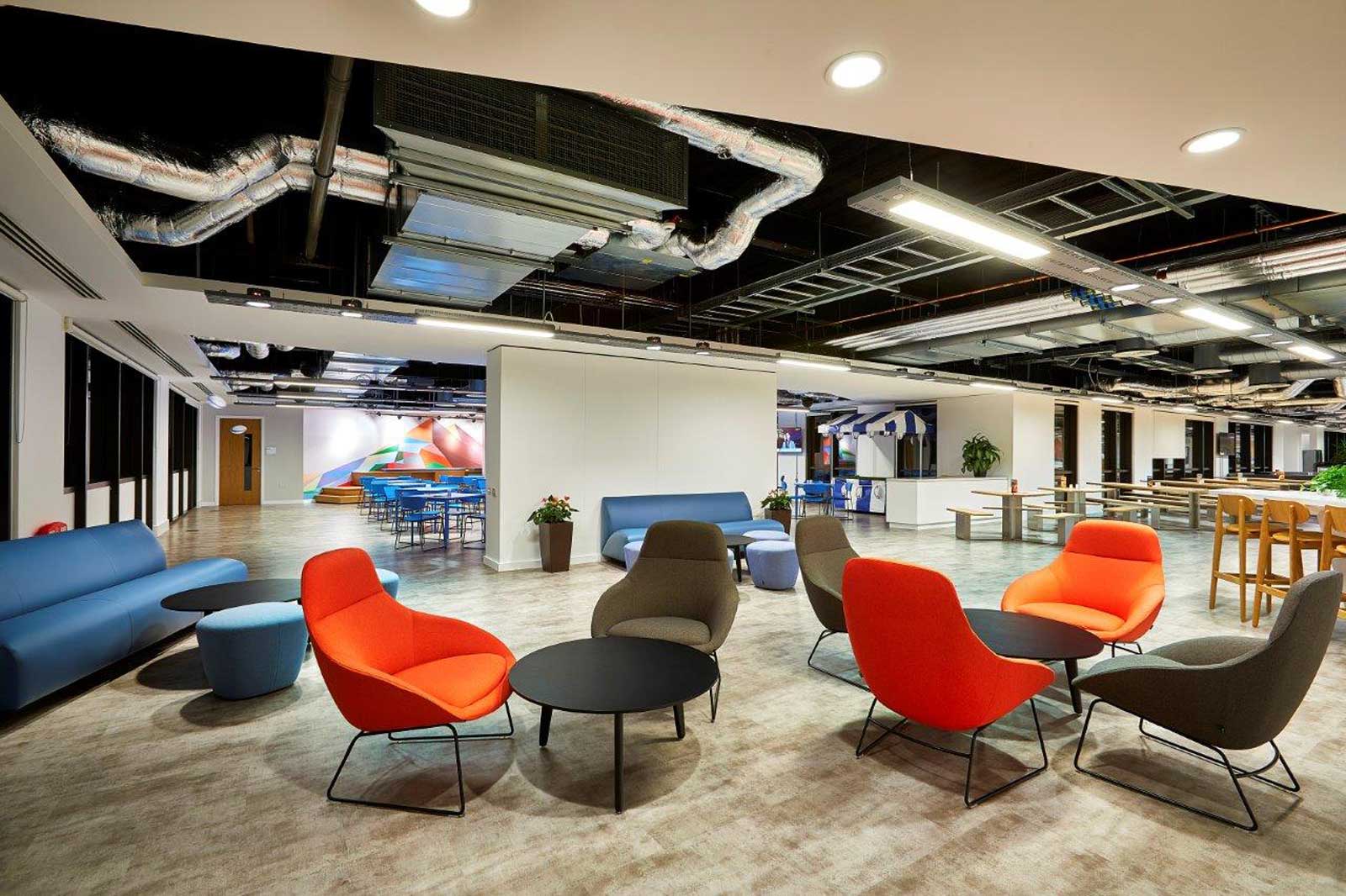 A modern office space featuring colourful chairs, sofas, and tables, with an open layout and decorative walls.
