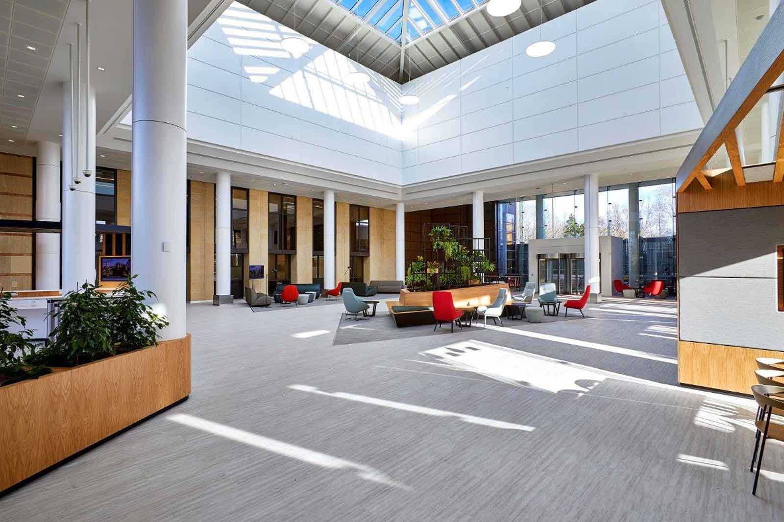 A spacious modern lobby with a high ceiling, large windows, and various seating options in vibrant colours.