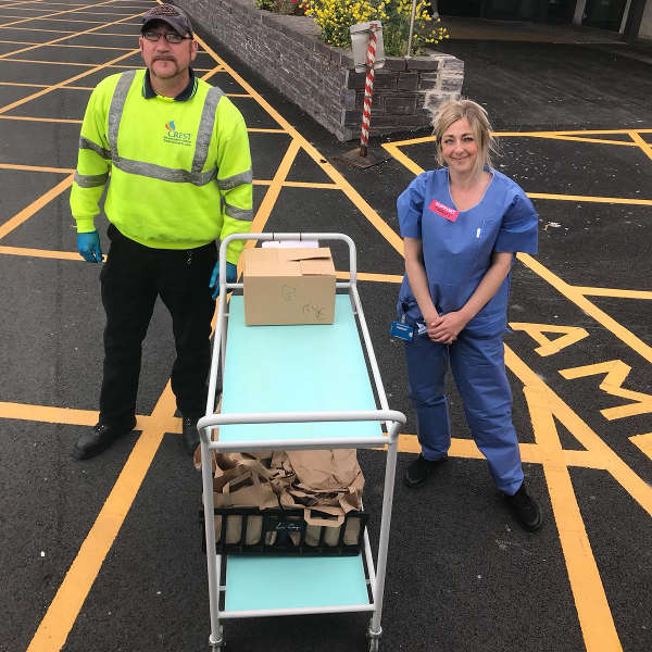 Two people stand next to a cart with a box and bags, on a marked parking area with yellow lines.
