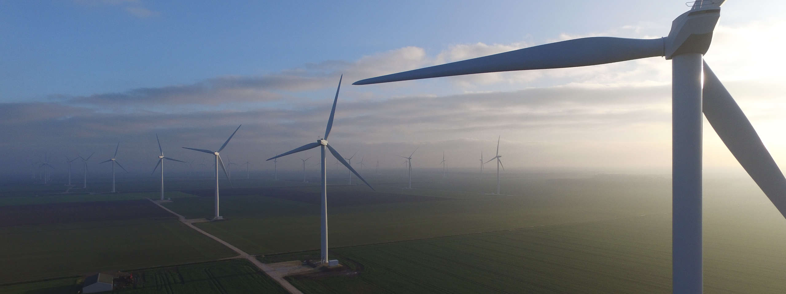 Aerial view of multiple wind turbines in a flat, expansive landscape under a cloudy sky, showcasing renewable energy.