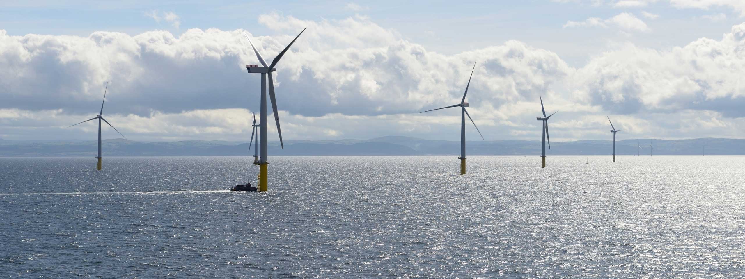 A serene view of offshore wind turbines under a partly cloudy sky, with a boat navigating the shimmering sea.