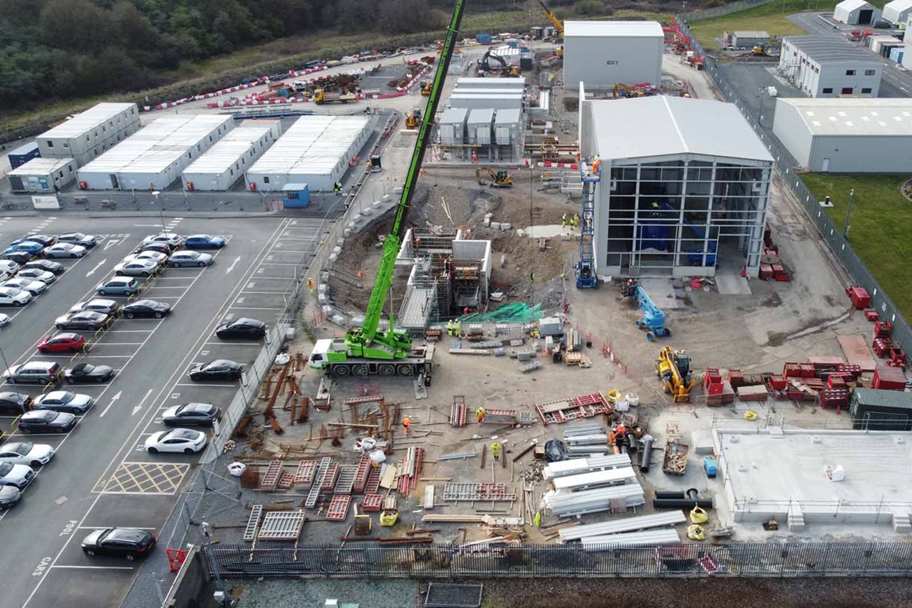 An aerial view of a construction site showing cranes, vehicles, and temporary buildings amidst ongoing construction work.