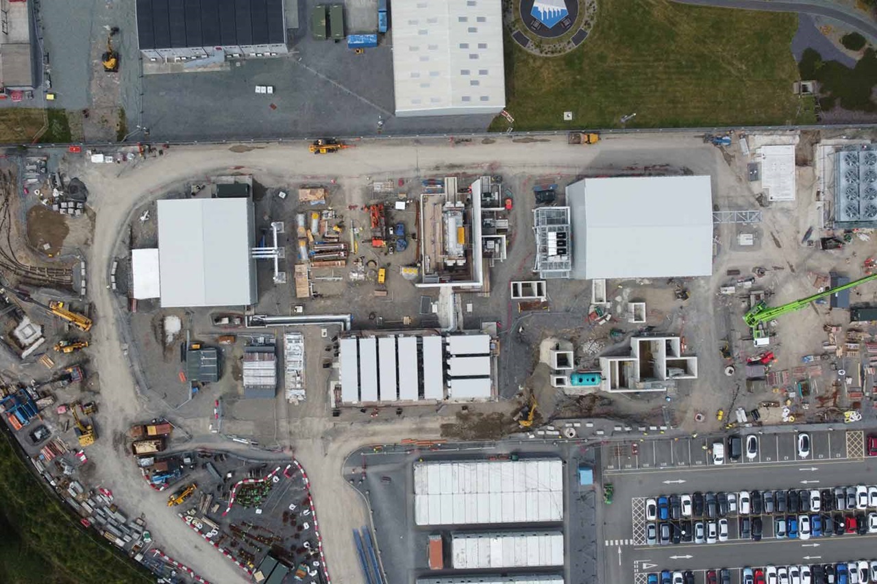 Aerial view of a construction site featuring various equipment, materials, and buildings under construction, with workers visible.