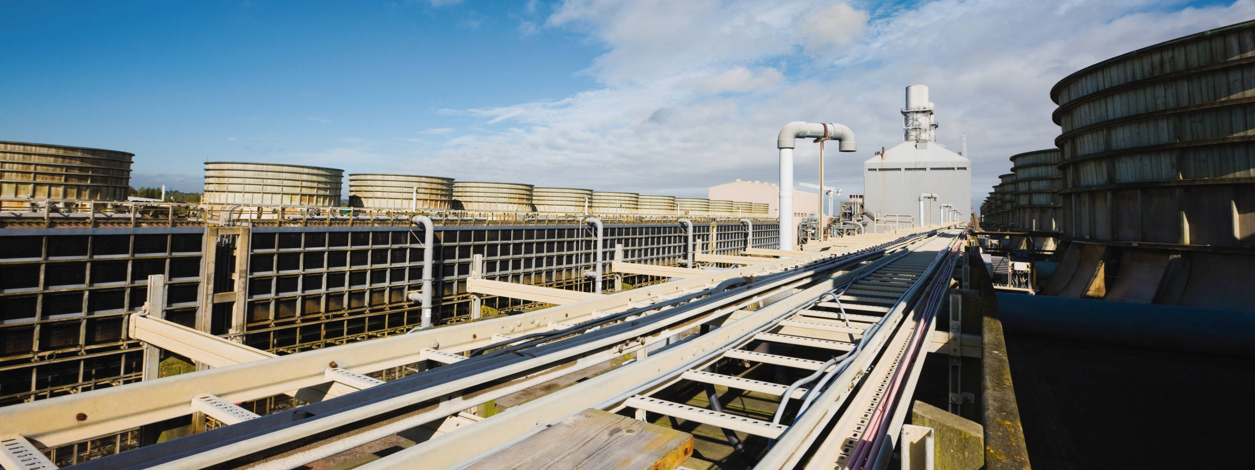 Industrial site featuring large cooling towers, piping, and a clear blue sky.