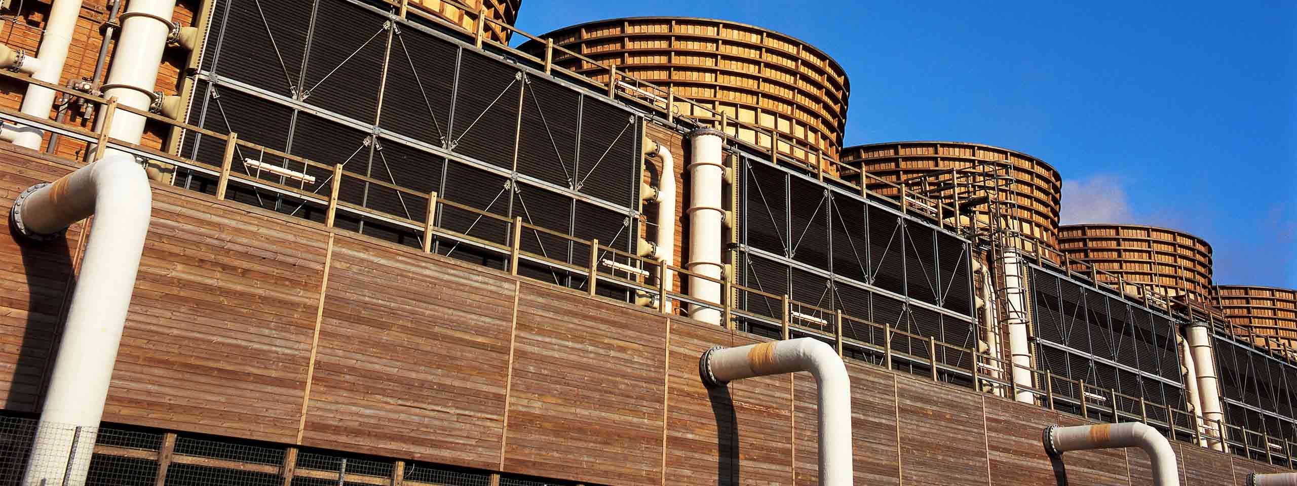 The image shows a cooling tower structure with wooden caps and large pipes against a blue sky.