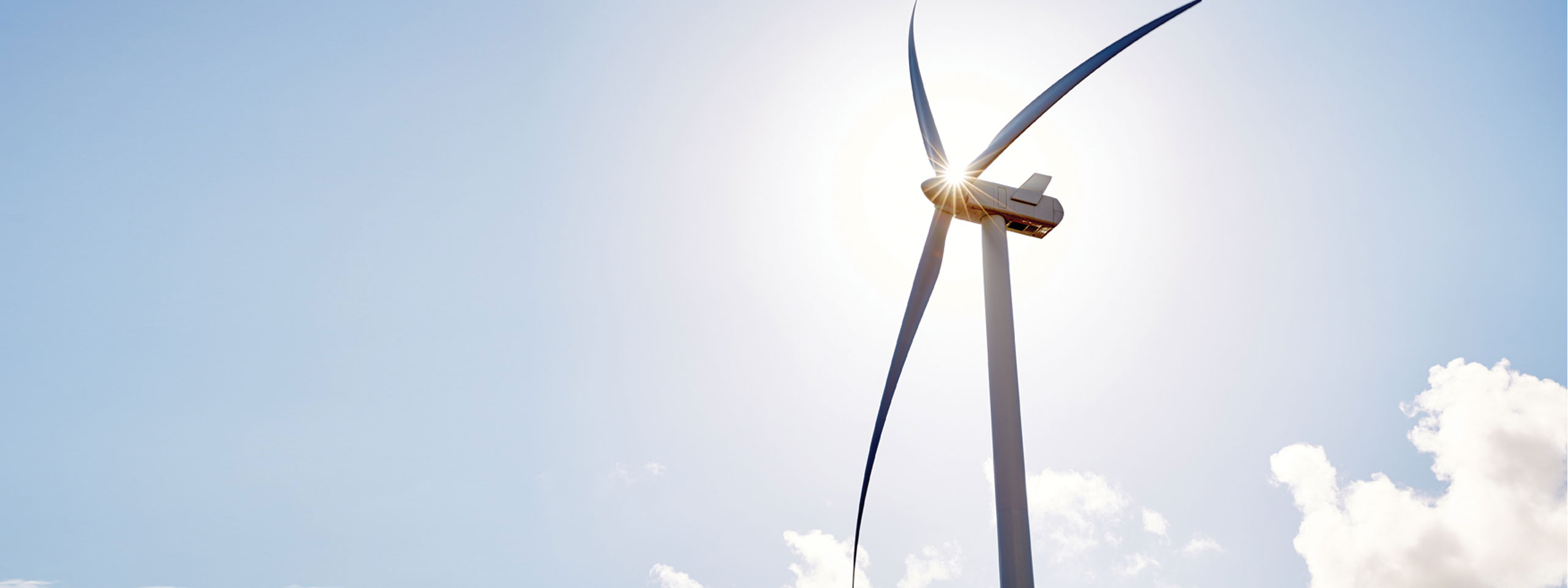 A tall wind turbine with three blades, set against a clear blue sky and bright sunlight.