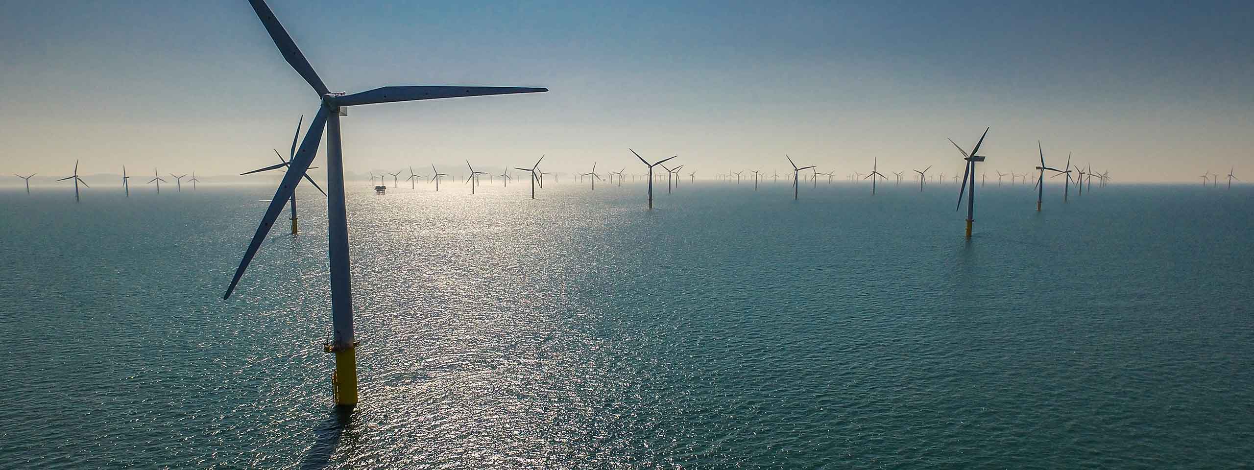 A serene view of offshore wind turbines standing tall in calm waters, reflecting sunlight under a clear sky.