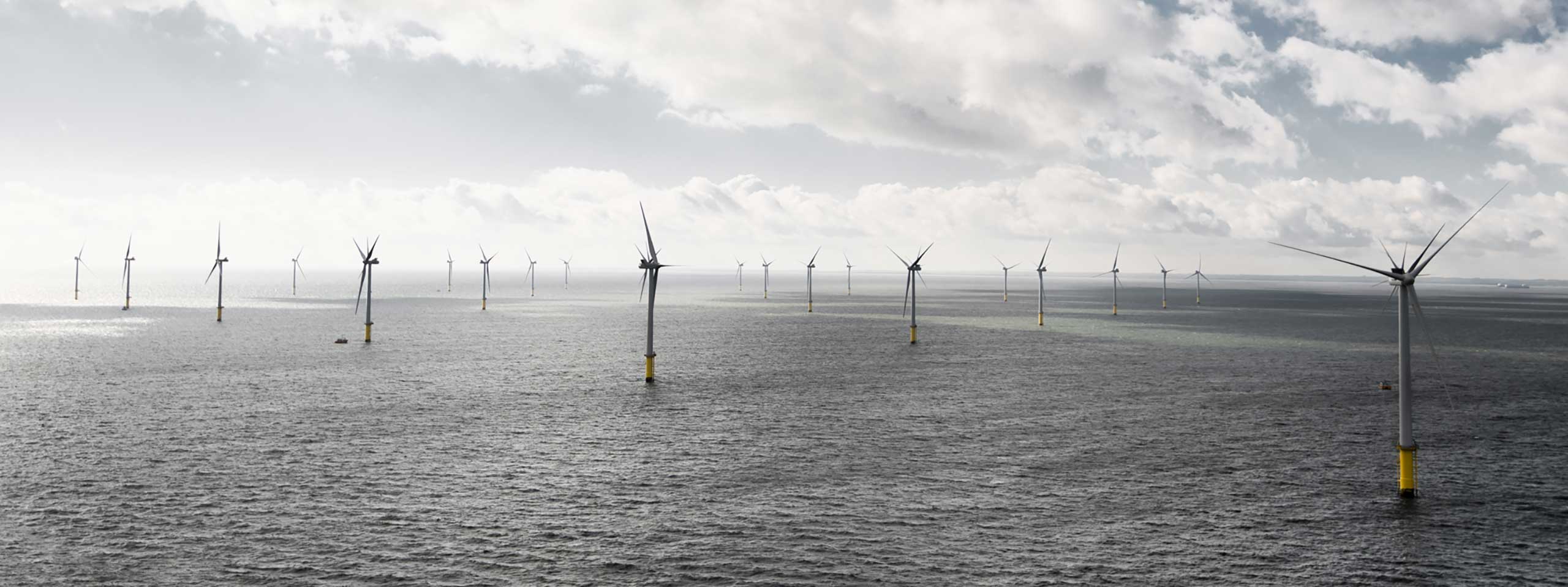 A panoramic view of offshore wind turbines in the sea under a cloudy sky.