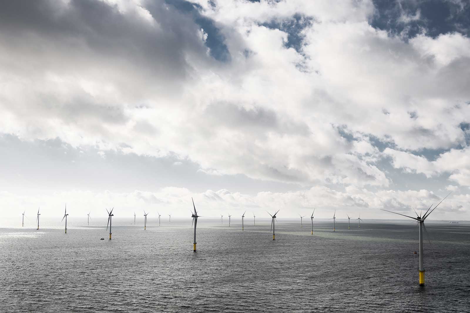 A panoramic view of wind turbines in the sea, surrounded by cloudy skies and gentle waves.