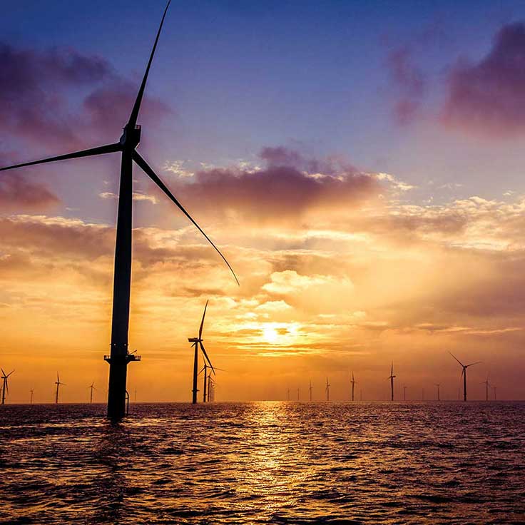 Wind turbines silhouetted against a vibrant sunset over the ocean, creating a serene and sustainable energy scene.