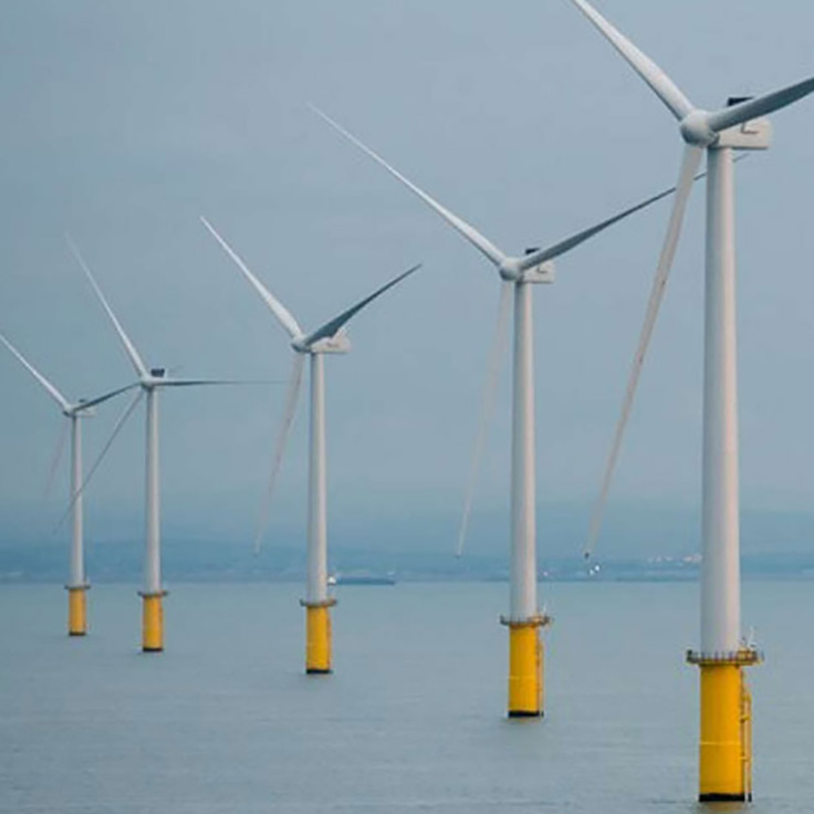 Offshore wind turbines standing tall in the ocean, with yellow foundation visible against a cloudy sky.