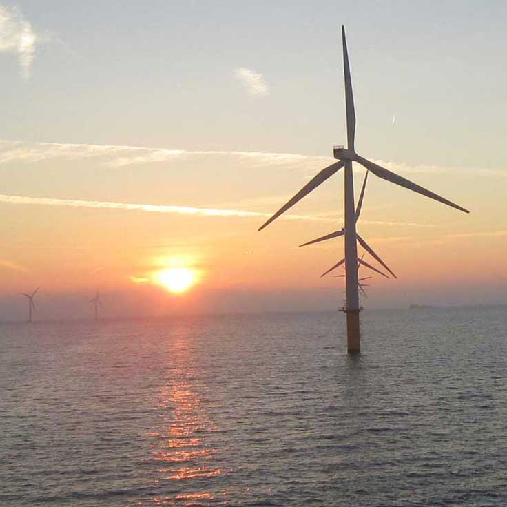 A scenic view of offshore wind turbines at sunset over calm waters, with colourful clouds in the sky.