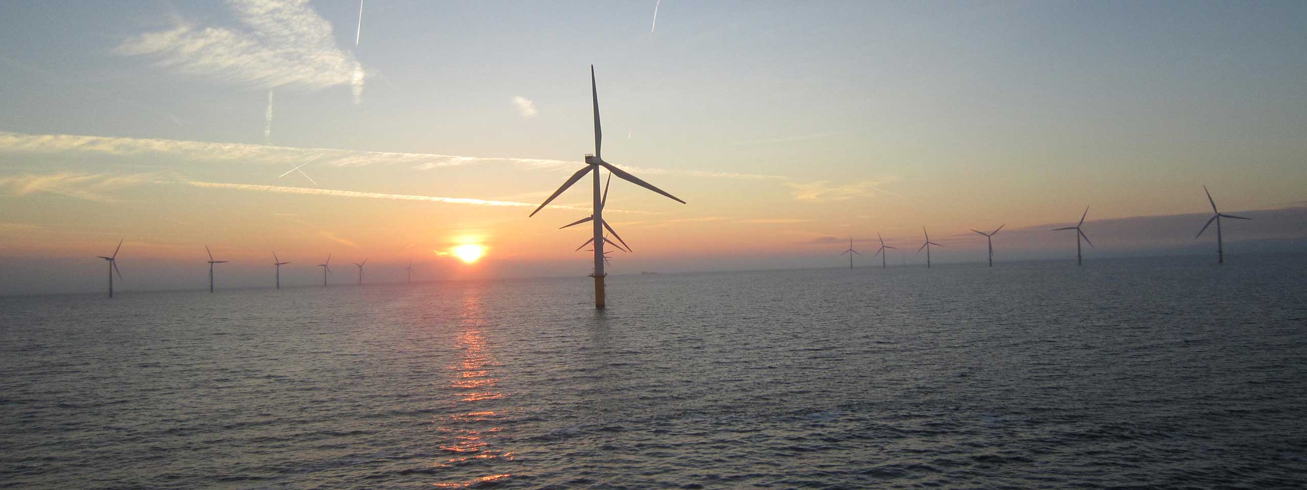 A serene seascape featuring several wind turbines silhouetted against a vibrant sunset over the water.