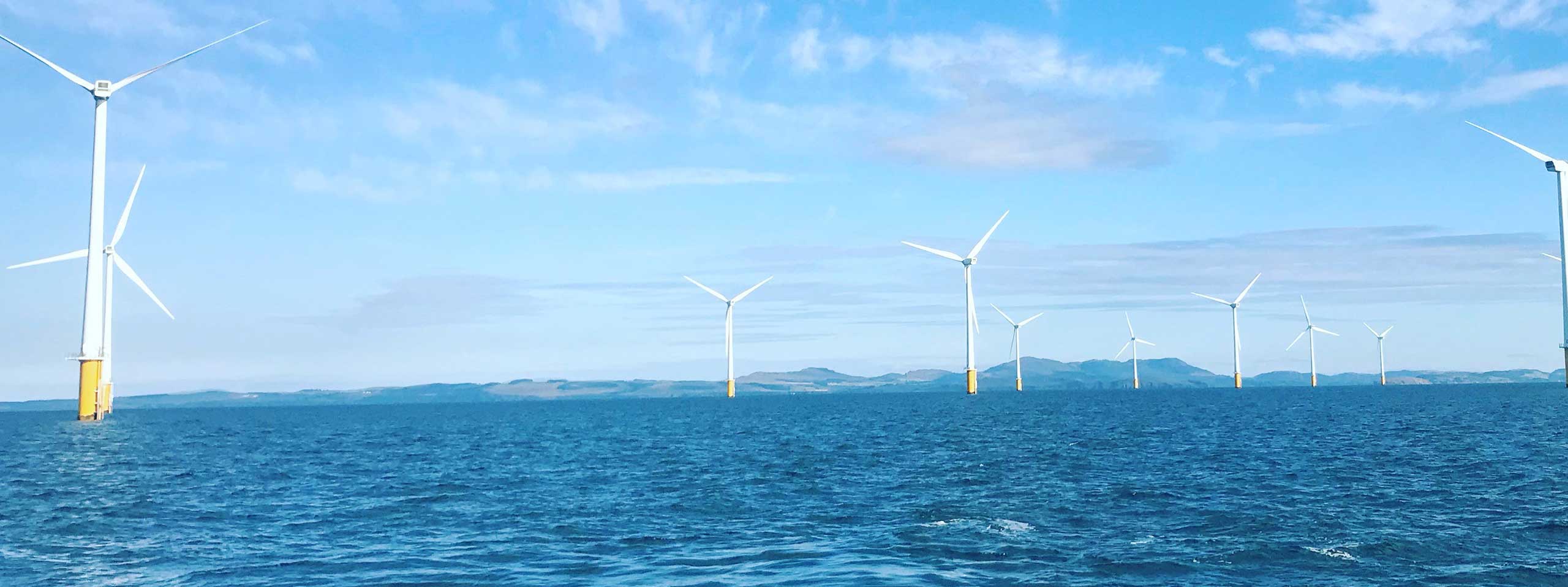 A scenic view of offshore wind turbines standing in the blue sea under a clear sky.