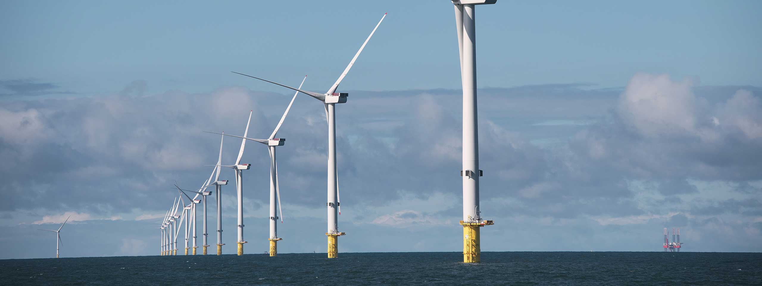 A landscape of offshore wind turbines standing tall in the ocean under a cloudy sky, showcasing renewable energy technology.