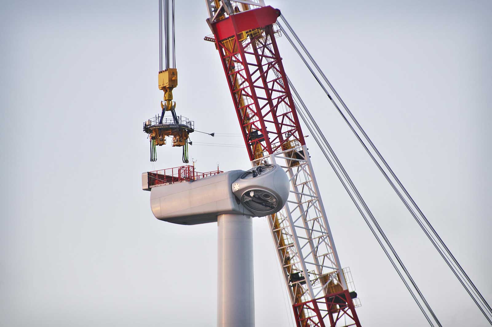 A crane hoists the top of a wind turbine, with its sleek body and rotor visible against a clear sky.