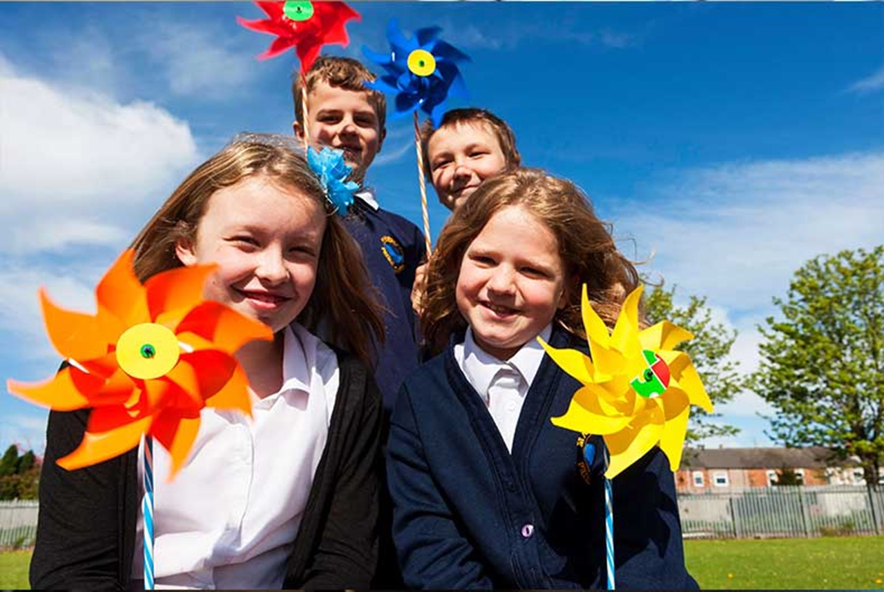 Group of children holding colourful pinwheels in a sunny outdoor setting.