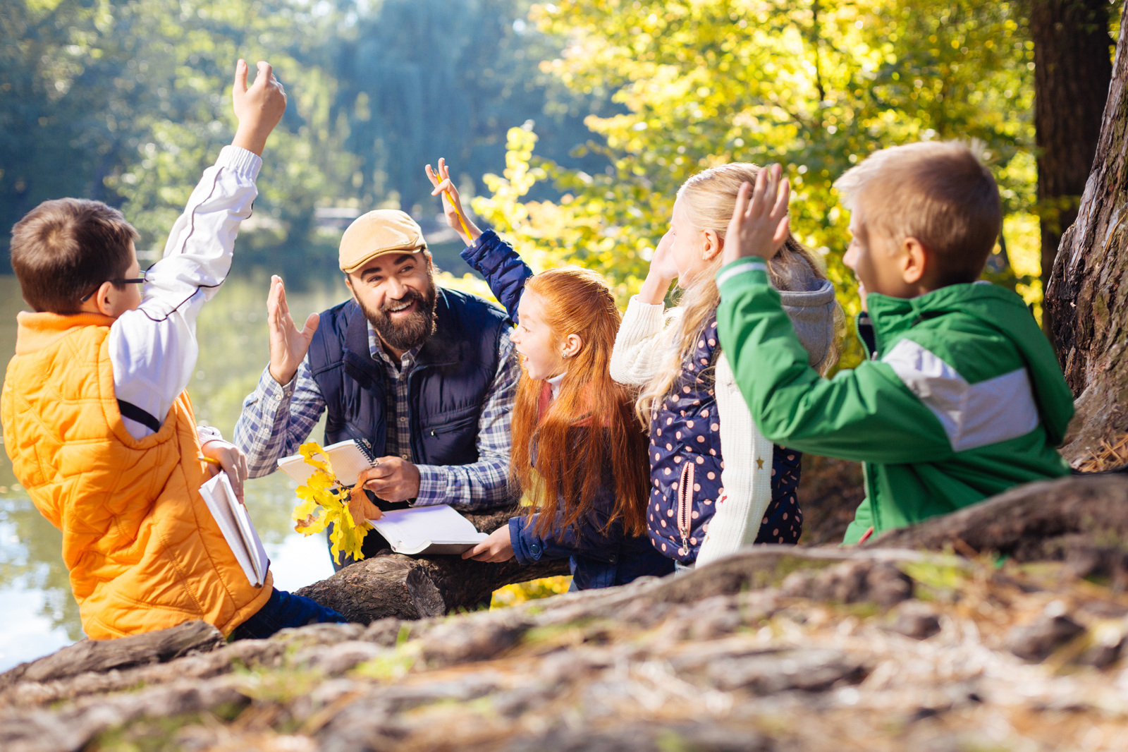 A group of children enthusiastically engaging in a learning activity outdoors beside a serene lake, surrounded by trees.
