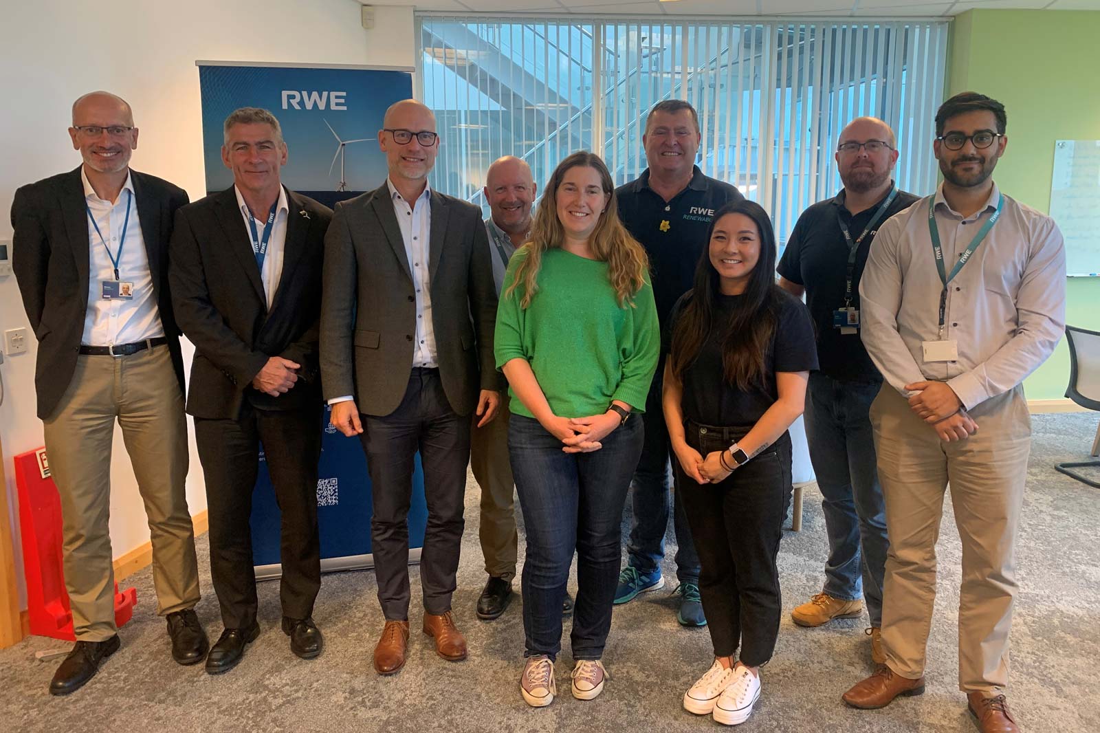 A group of eight individuals poses for a photo in an office setting, with RWE branding in the background.