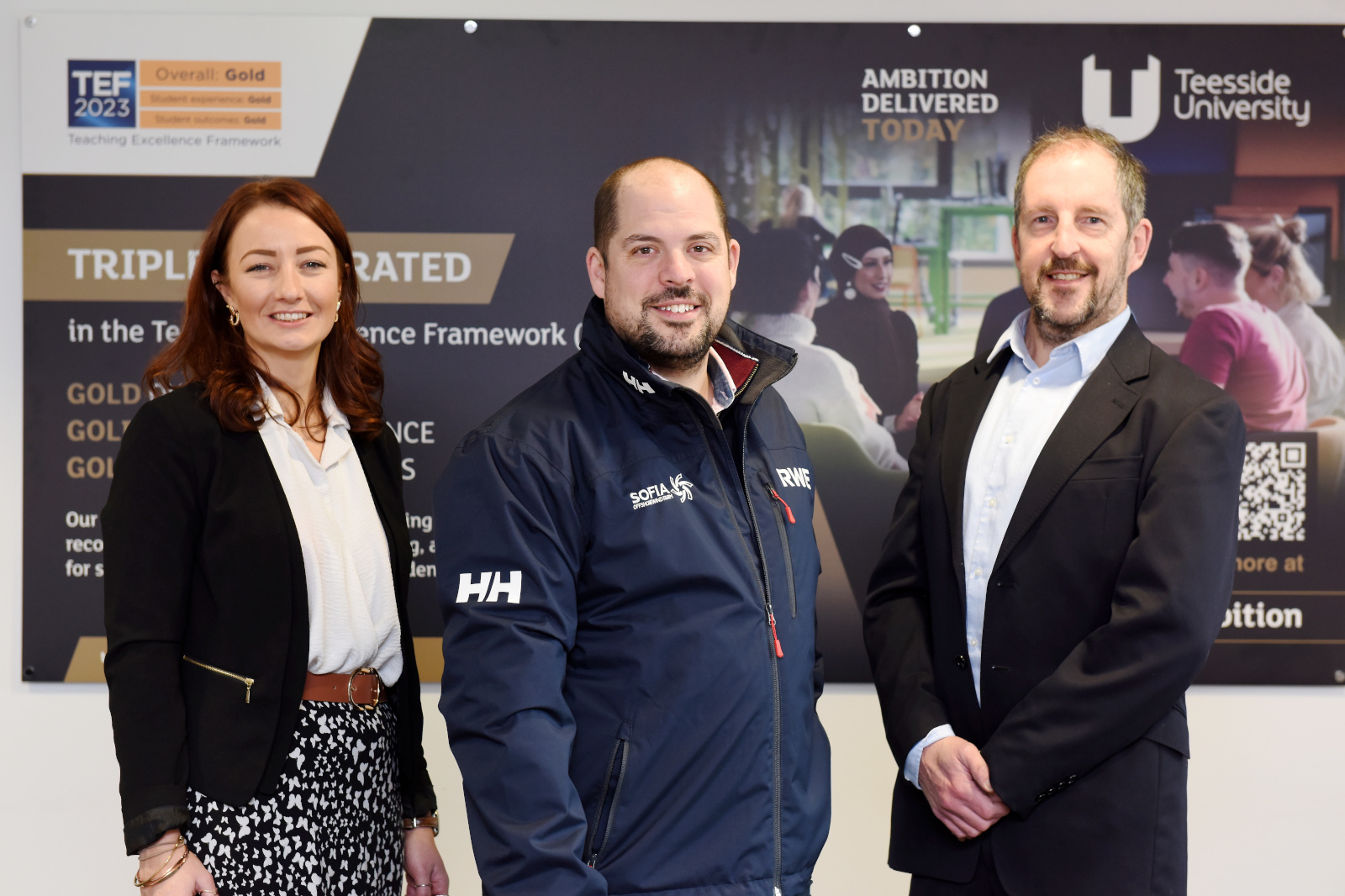 Three individuals stand in front of a Teesside University banner