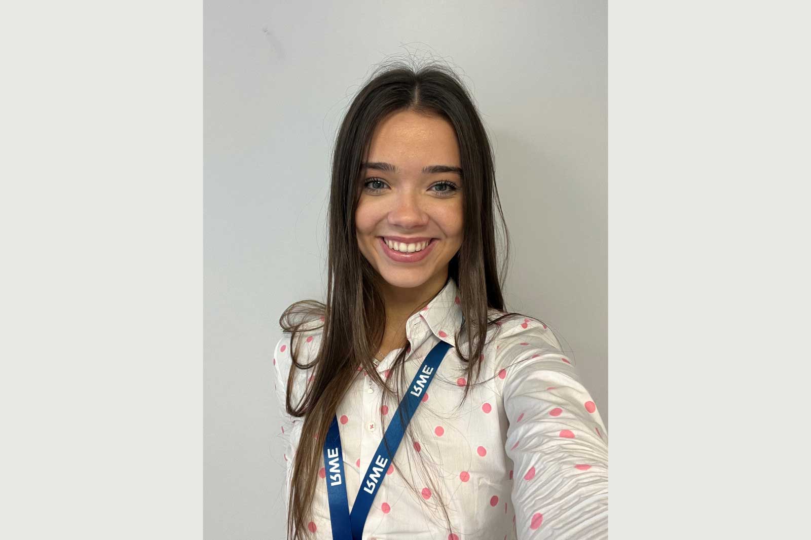 A person wearing a pink polka dot shirt and a blue lanyard, posing against a plain background.