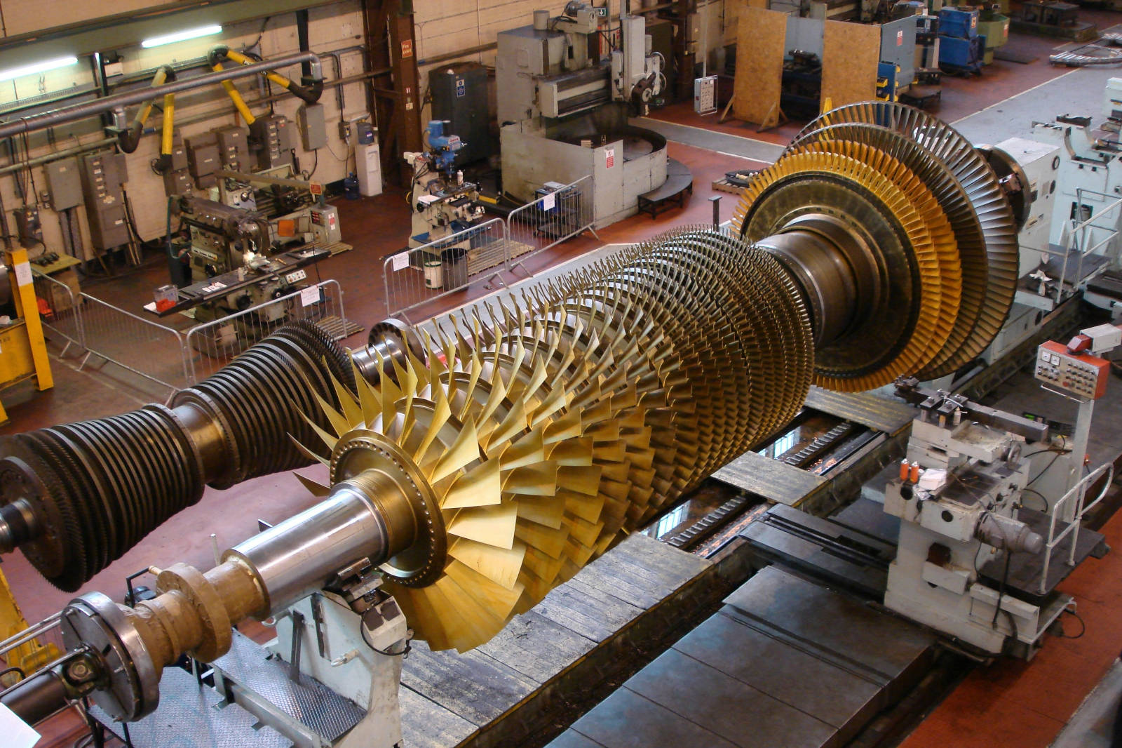 A large industrial gas turbine with golden blades, situated in a workshop with various machines in the background.