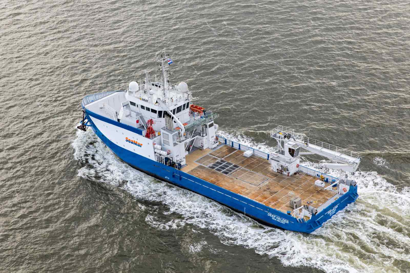 A blue and white research vessel named 'Deep Helder' navigates through rippling waters, showcasing its deck and equipment.
