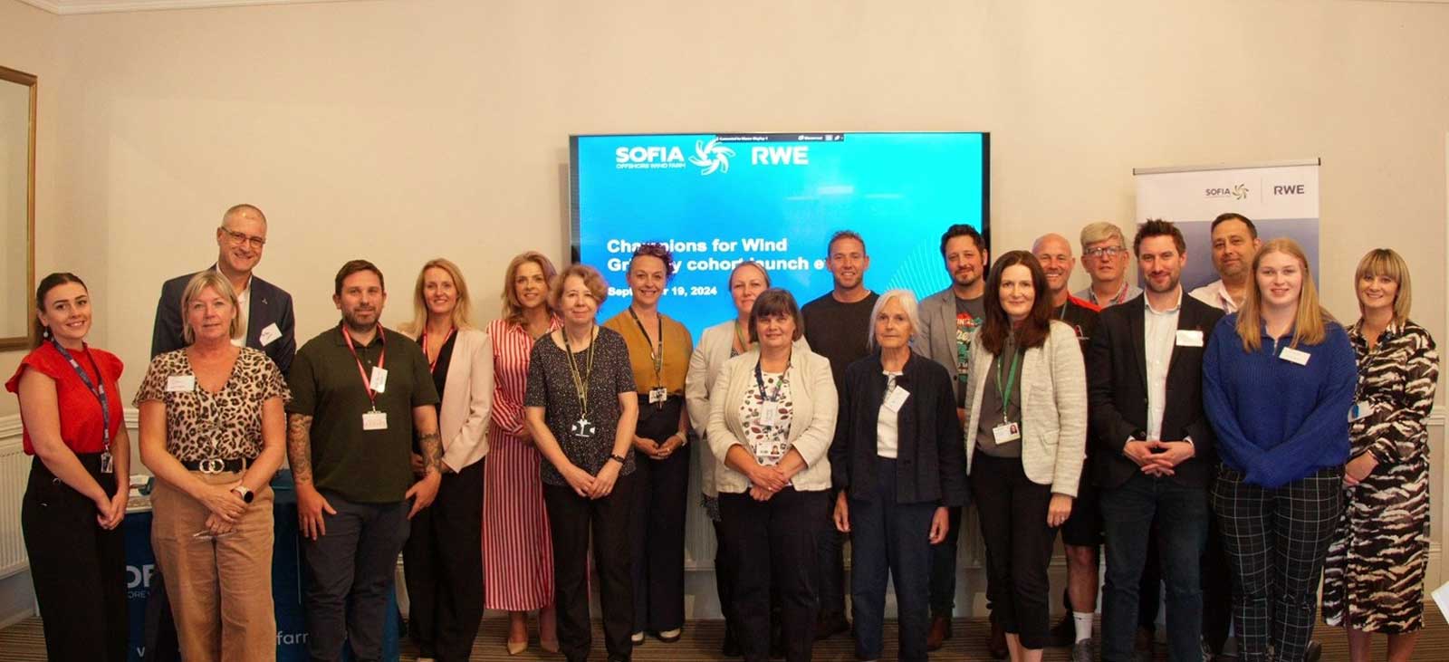 A group of people gathered in front of a presentation screen displaying 'Champions for Wind' event details.