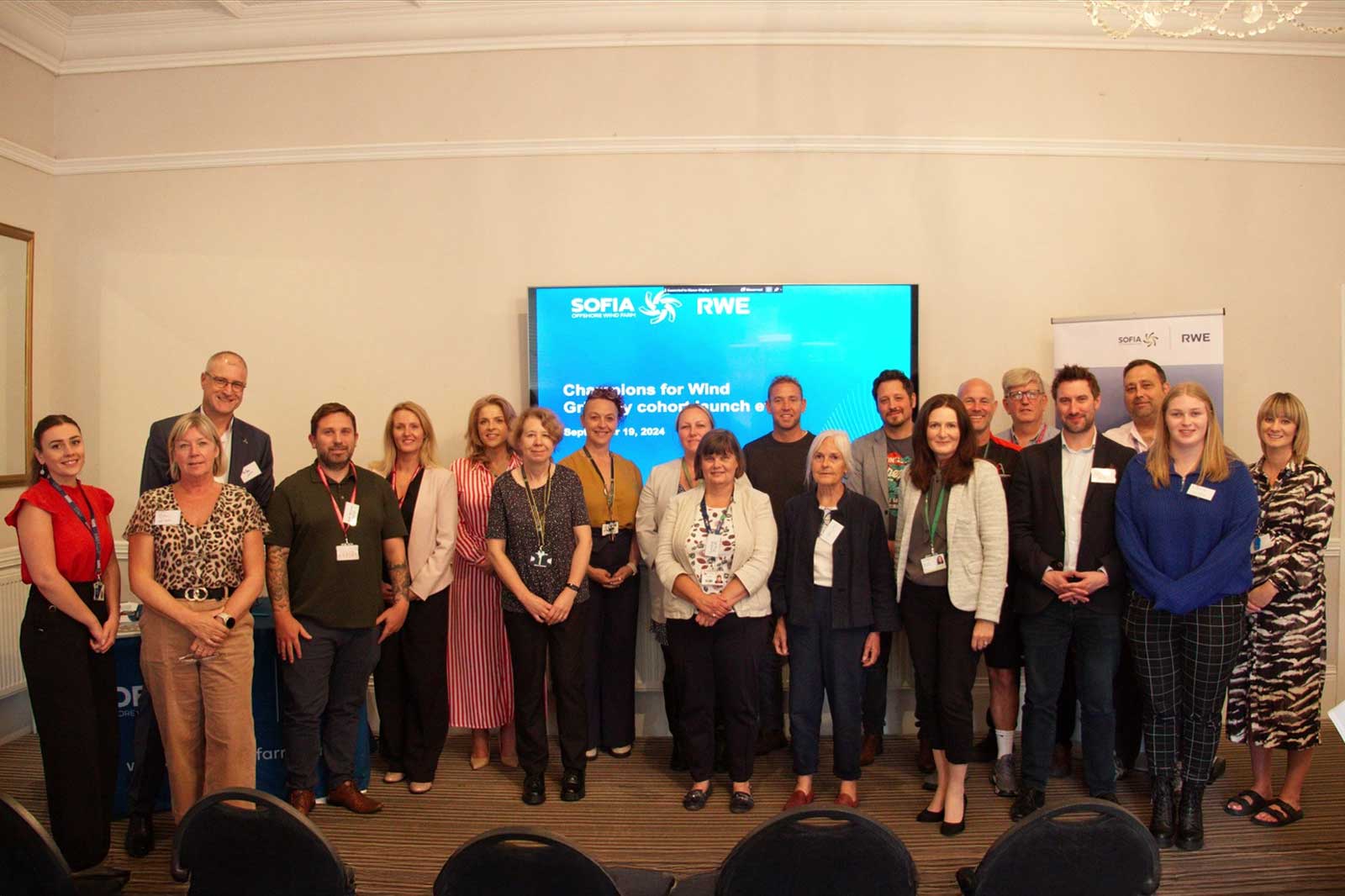 A diverse group of professionals gathered for a launch event, posing in front of a screen displaying the Sofia and RWE logos.