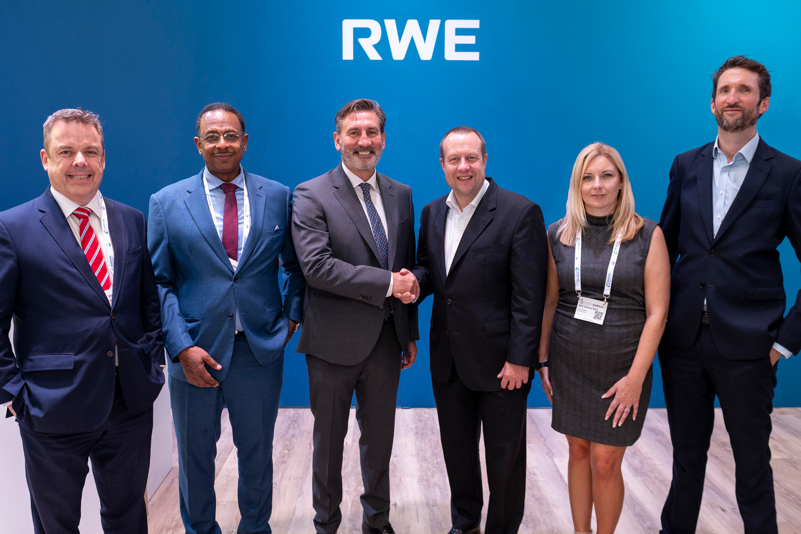 Group of professionals posing together, shaking hands in front of a blue background displaying the RWE logo.