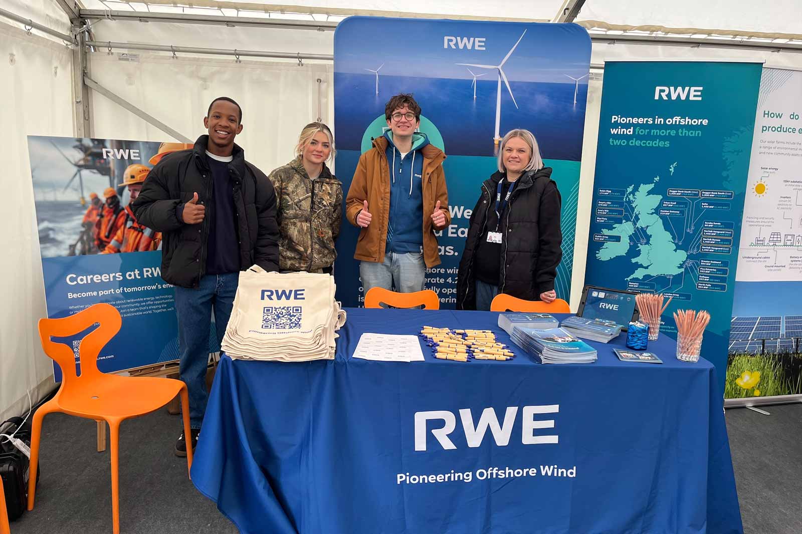 A group of four individuals stands in front of an RWE booth, showcasing offshore wind energy careers and resources.