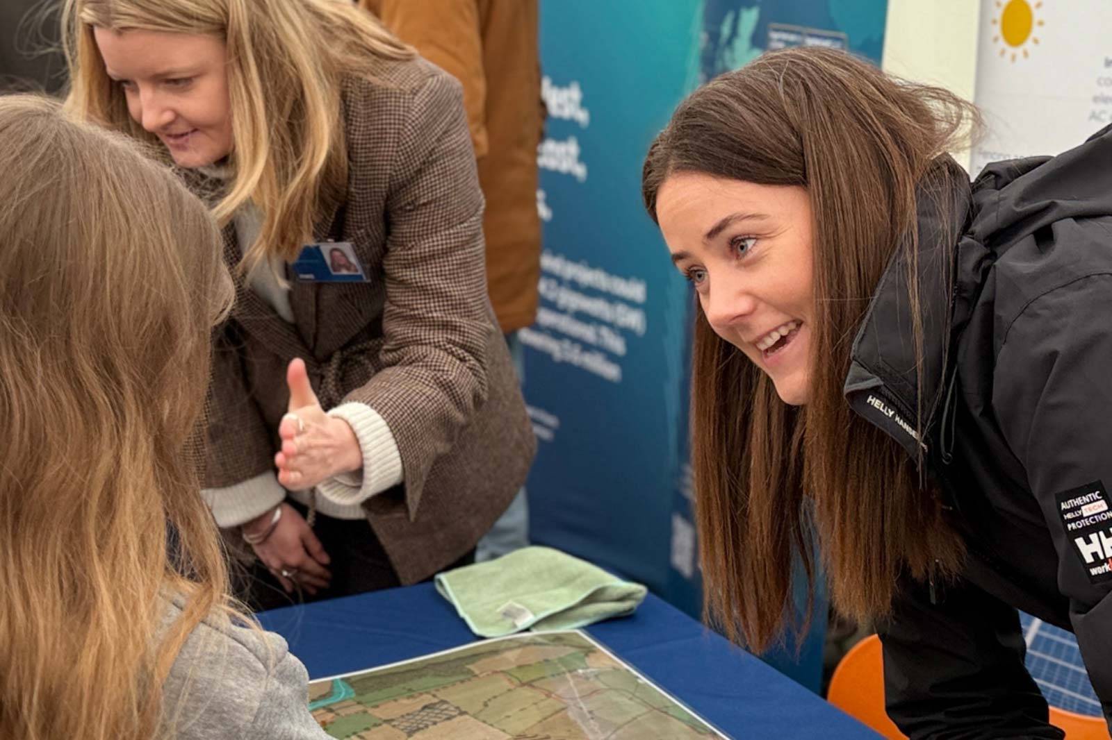 Two women engage in a discussion over a detailed map placed on a table, surrounded by a professional setting.