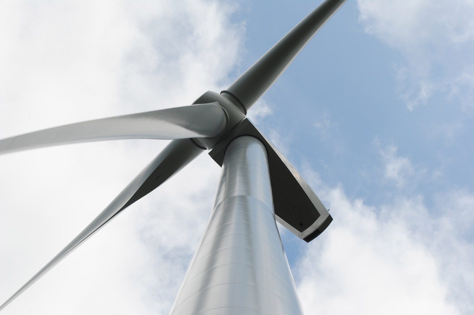 A close-up view of a wind turbine's blades and tower against a cloudy sky, showcasing renewable energy technology.
