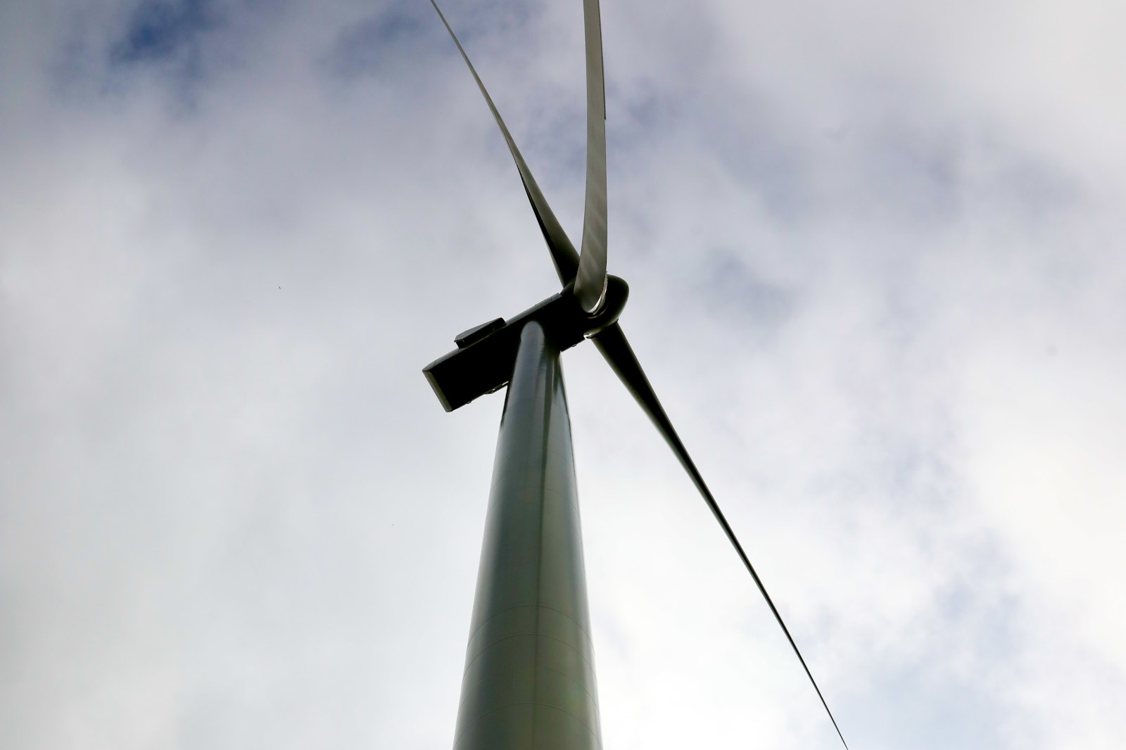 A low-angle view of a wind turbine against a cloudy sky, showcasing its tall structure and blades.