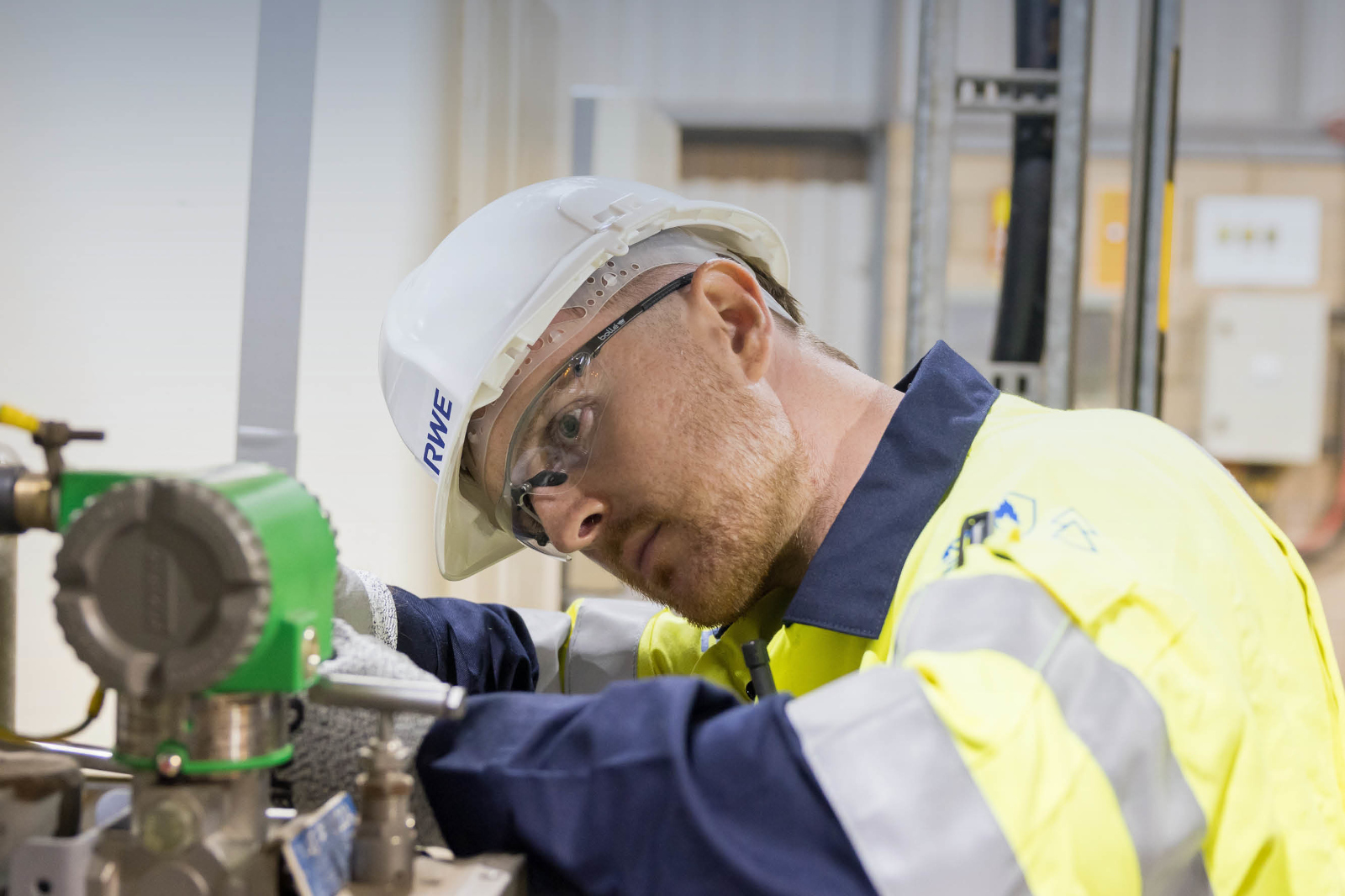 A worker in a safety helmet and high-visibility jacket is focused on machinery, demonstrating a professional work environment.