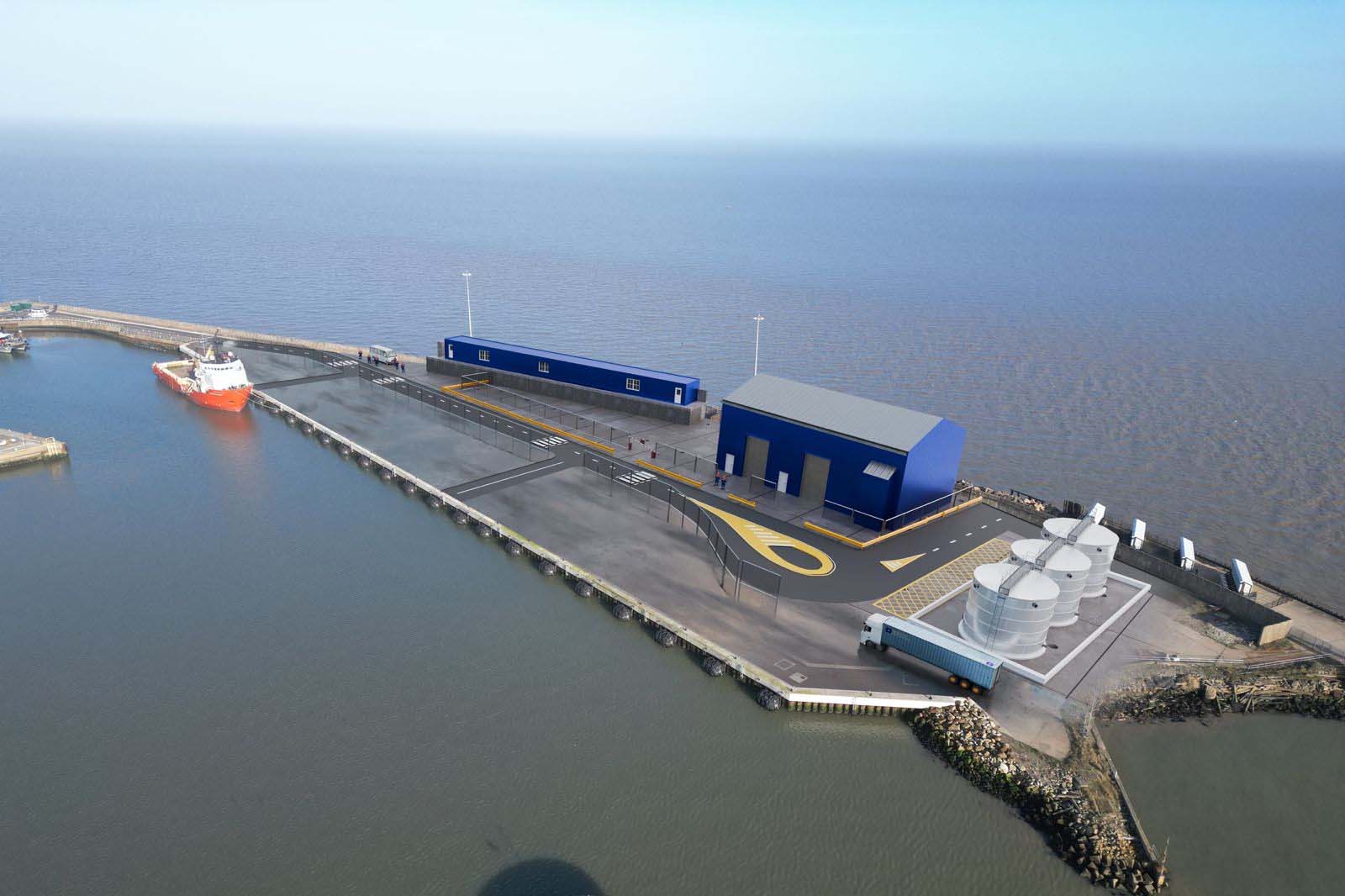 Aerial view of a concrete harbour pier with blue warehouses, white storage silos, a parked truck and an orange ship moored at the quay.