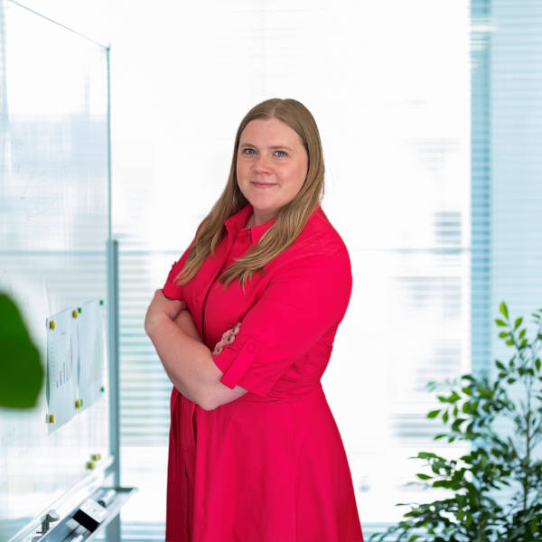 A person stands confidently with arms crossed, wearing a bright red dress in a modern office space with natural light.