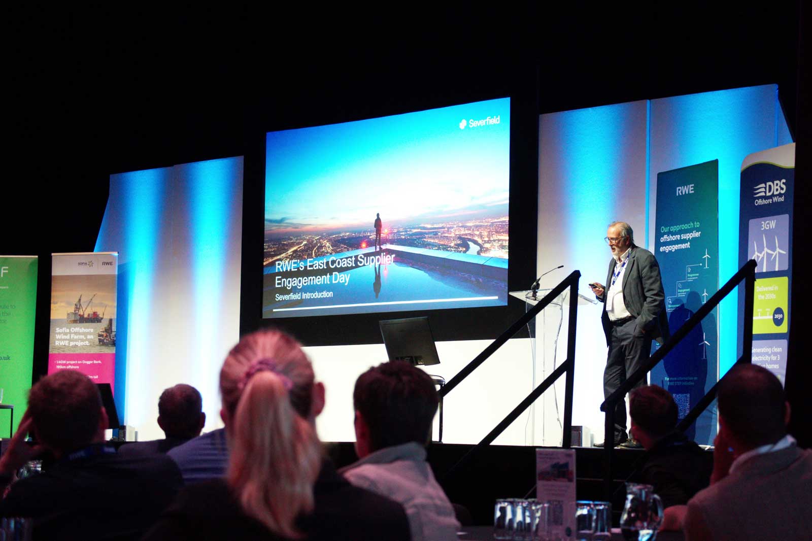 A speaker presents at RWE's East Coast Supplier Engagement Day, with a digital screen showcasing a landscape image.