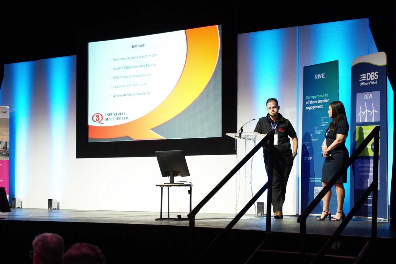 A presentation scene featuring two speakers beside a screen displaying key points about industrial supplies and offshore servicing.